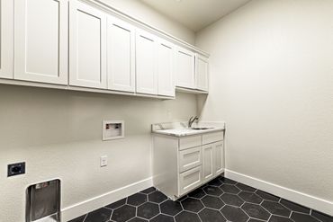 Modern laundry room with white cabinetry and black hexagon tile flooring.