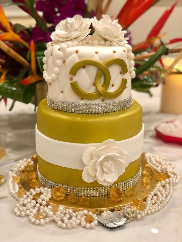 Two tier white and gold Channel cake with three white flowers and white pearls.