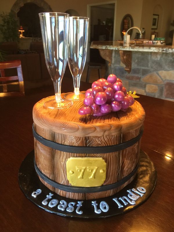 Wine barrel cake with sugar grapes and plastic flute glasses on top.
