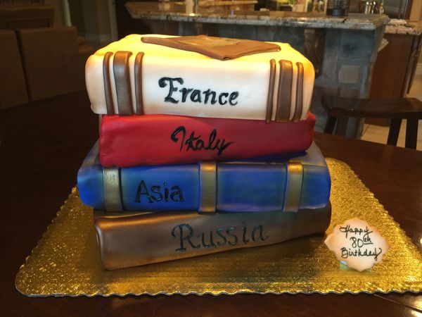 Cake of 4 travel books stacked on top of one another with passport on top