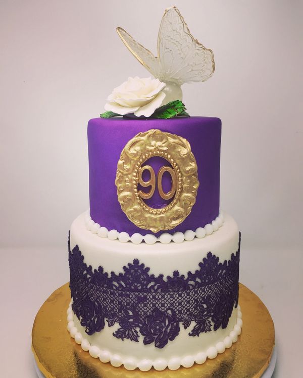 Two tier purple and white cake with a white flower and clear sugar butterfly on top.