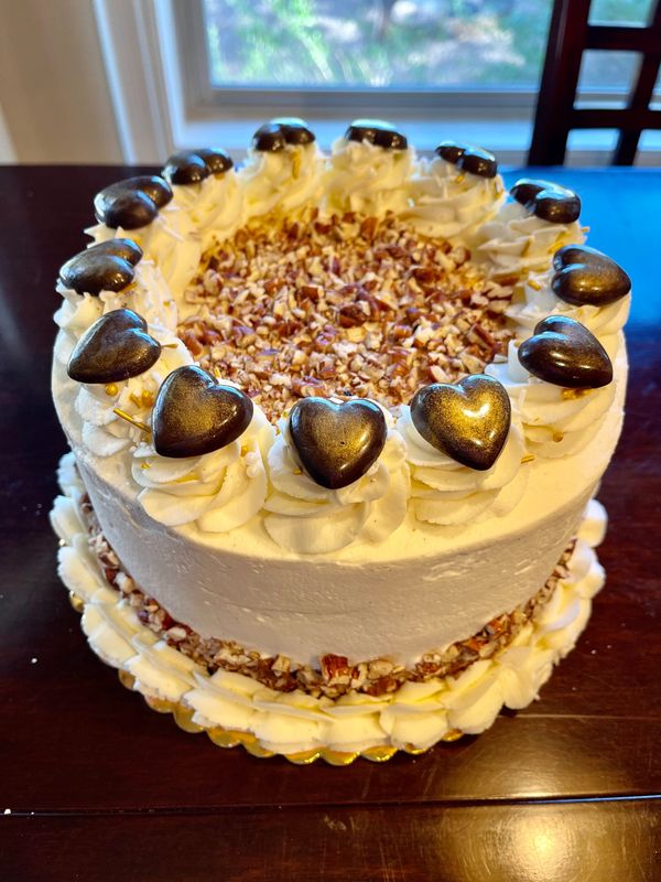 white cake with white rosettes, gold hearts and pecans