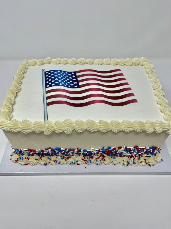 White cake with a red, white and blue waving American flag on top, with sprinkles on the side.