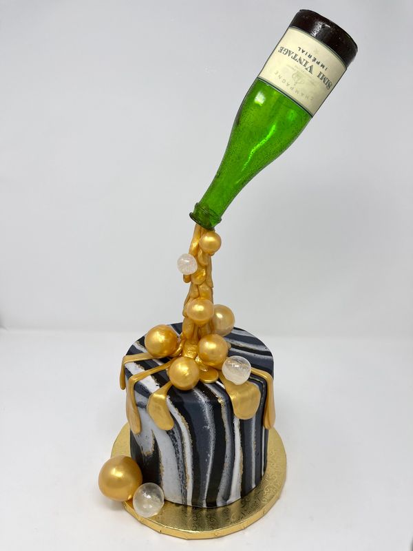 Black and white cake with champagne bottle pouring gold bubbles on cake