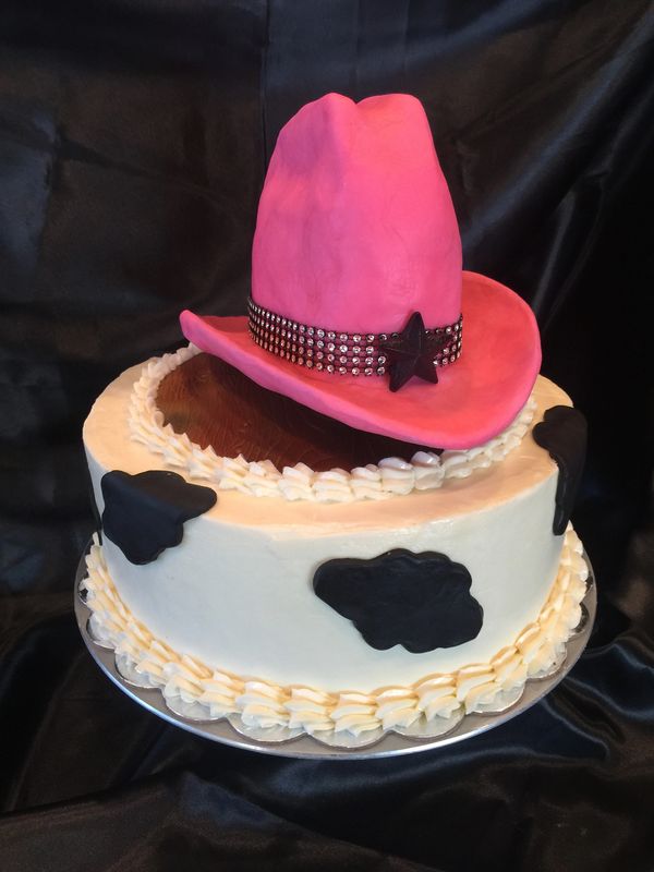 pink cowboy hat on top of a white cake with black cow spots on it