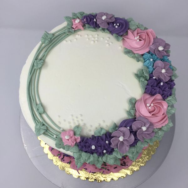 white cake with wreath on top with pink, blue, purple and lavender flowers