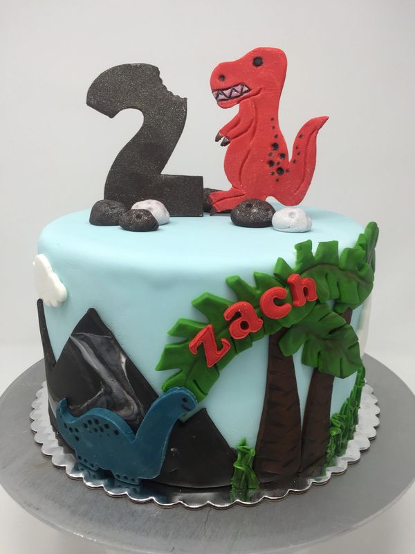 Blue cake with dinosaurs and palm trees and mountains