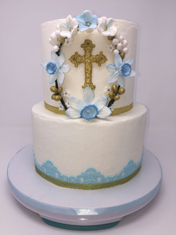 White cake two tiers with blue and white daffodils  wreath around a gold cross