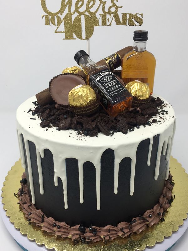 Black cake with White chocolate drip and candy and whiskey bottles on top.