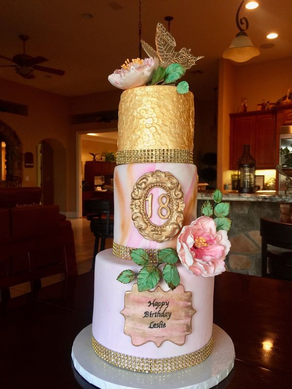 3 tier gold and pink cake with pink sugar flowers and a clear butterfly on top.