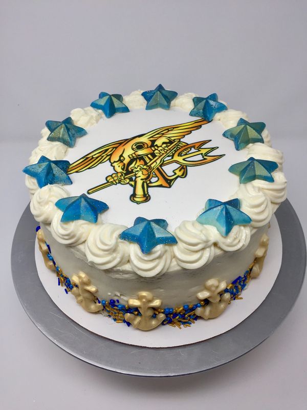 white cake with navy seal logo on top gold anchors and blue stars