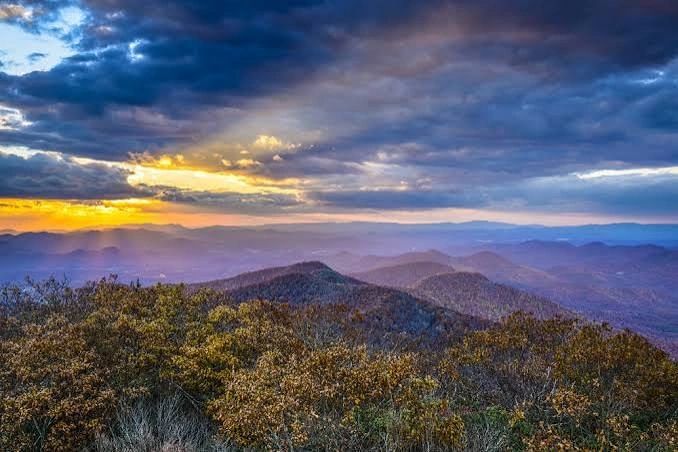 Sunset over rolling mountains with autumn foliage and dramatic clouds.