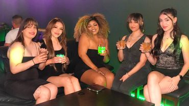 Five women dressed in black enjoy drinks together in a dimly lit lounge.