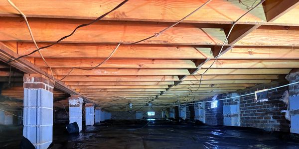 Crawl space under a house with wooden beams and concrete block supports.