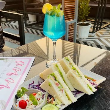 Blue drink with a plate of fresh sandwiches on a table at sunset.