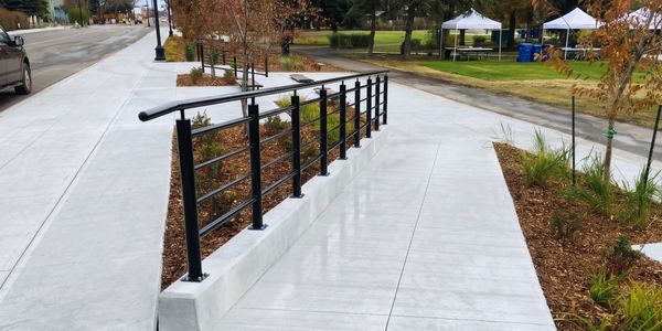 Modern black metal handrail on a concrete sidewalk with autumn foliage.