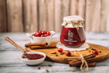 Jar of cranberry sauce with fresh cranberries and cinnamon sticks on a wooden board.