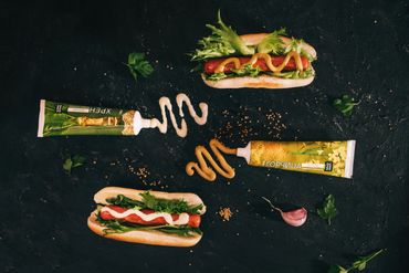 Two hot dogs with lettuce and sauces from tubes on a dark surface.