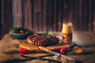 Grilled steak with mustard, cherry tomatoes, and greens on rustic paper.