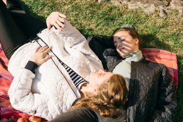 Two women lying on a blanket outdoors, enjoying the sunlight with eyes closed.