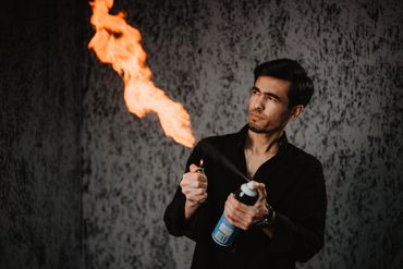 Man creating a large flame using a lighter and spray can indoors.
