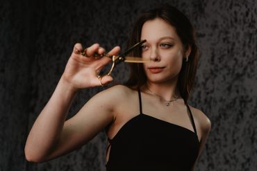 Young woman holding golden hair thinning scissors in focus.