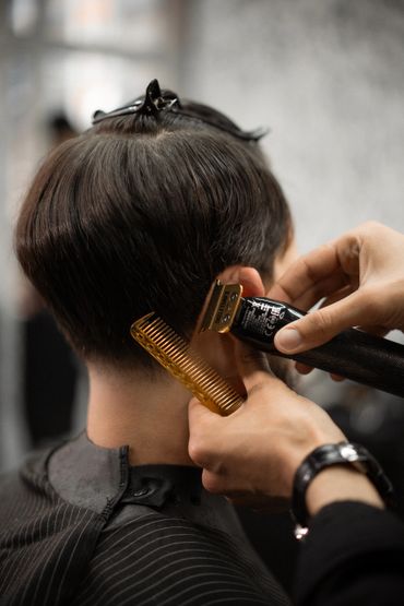 Barber trimming hair with clippers and comb at a salon.
