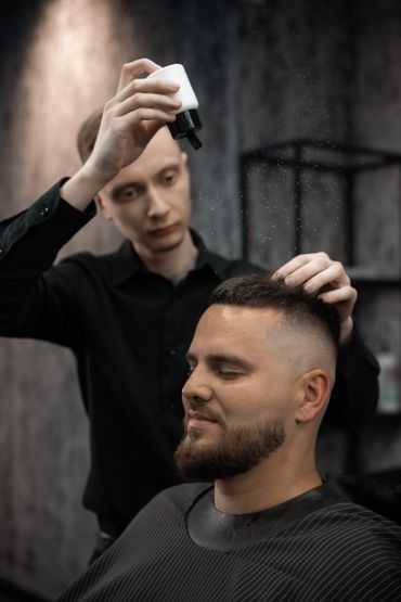 Barber applying hair product to client's freshly cut hair in a modern salon.