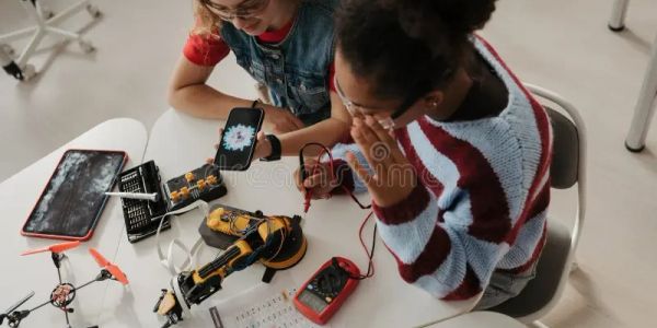 Two girls working on a robotics project with tools and devices on a table.