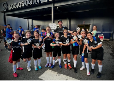 Youth soccer team proudly holding trophies and posing with their coach after a match.