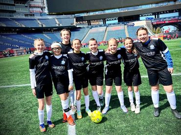 Young girls' soccer team posing on a stadium field, smiling and ready to play.