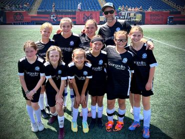 Youth soccer team posing on the field with their coach in black uniforms.