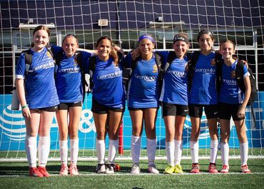 Youth girls soccer team in blue jerseys posing in front of goal net.