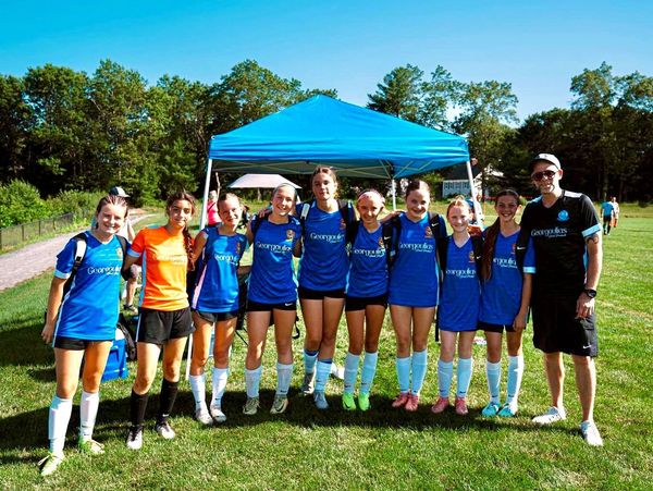 Youth soccer team posing together on a sunny day under a blue canopy.