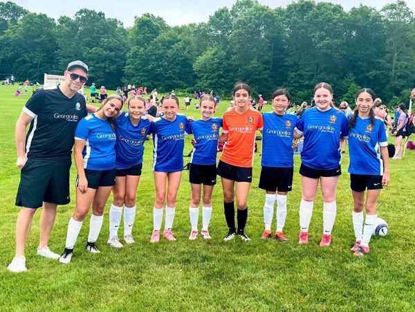 Youth soccer team posing together on a grassy field with their coach.