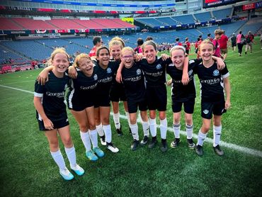 Young girls soccer team in black uniforms smiling on the field.