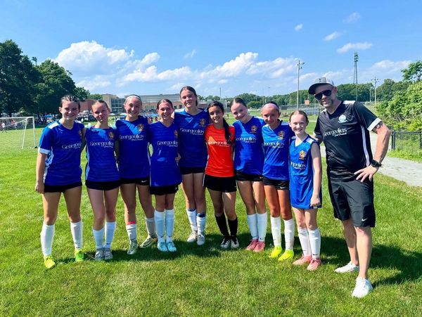 Youth soccer team in blue uniforms posing with their coach on a sunny day.