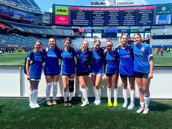 A group of young female soccer players posing at Gillette Stadium.