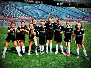 Young girls in black soccer uniforms posing happily on a soccer field.