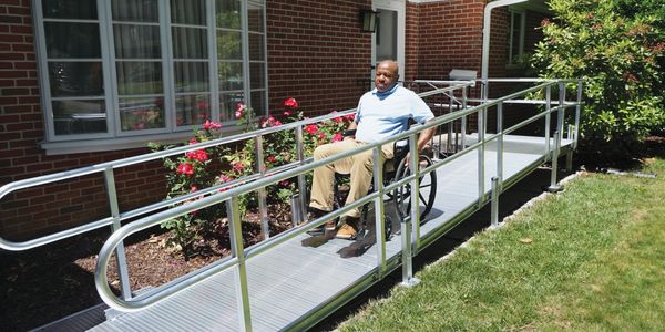 A man in a wheelchair using an outdoor ramp beside a brick building.