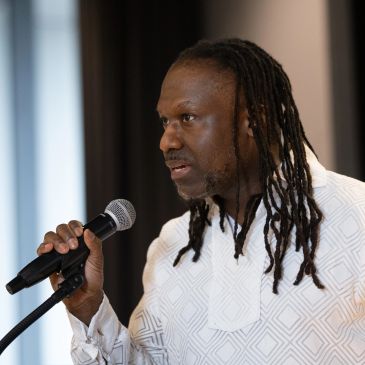 Man with dreadlocks speaking into a microphone.