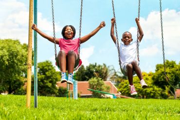 Two children joyfully swinging in a sunny park.