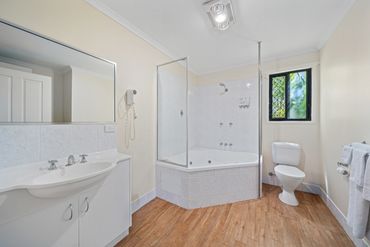 Bright bathroom with corner bathtub, white sink, and wood-look flooring.
