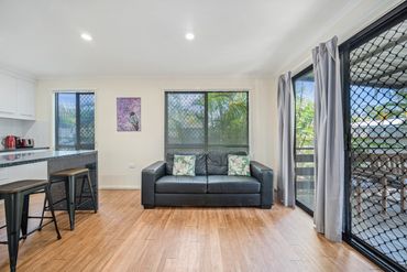 Bright living room with black leather sofa, wooden floor, and kitchen stools.