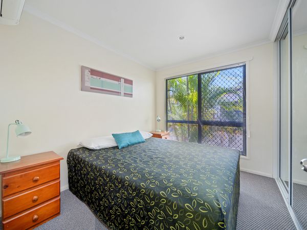 Bright bedroom with patterned bedspread and large window overlooking greenery.