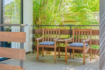 Two wooden chairs with cushions on a sunny balcony surrounded by greenery.
