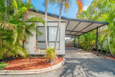 Modern house exterior with a carport and lush tropical plants.