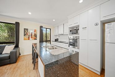 Modern kitchen with a large island, stainless steel sink, and white cabinetry.