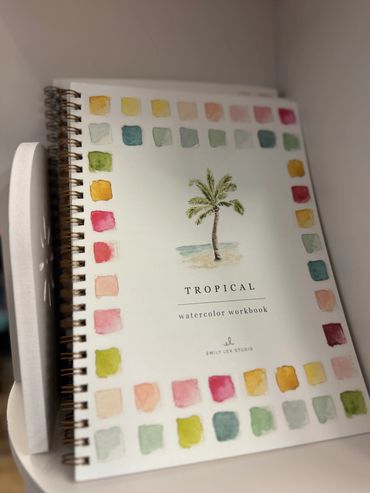 Tropical watercolor workbook with colorful paint swatches and palm tree illustration.