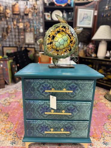 Decorative teal chest with intricate drawer patterns and turtle sculpture on top.
